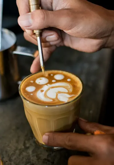 Hände gießen Latte Art in ein Glas