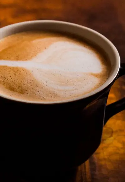 Cappuccino in einer dunklen Tasse im warmen Licht